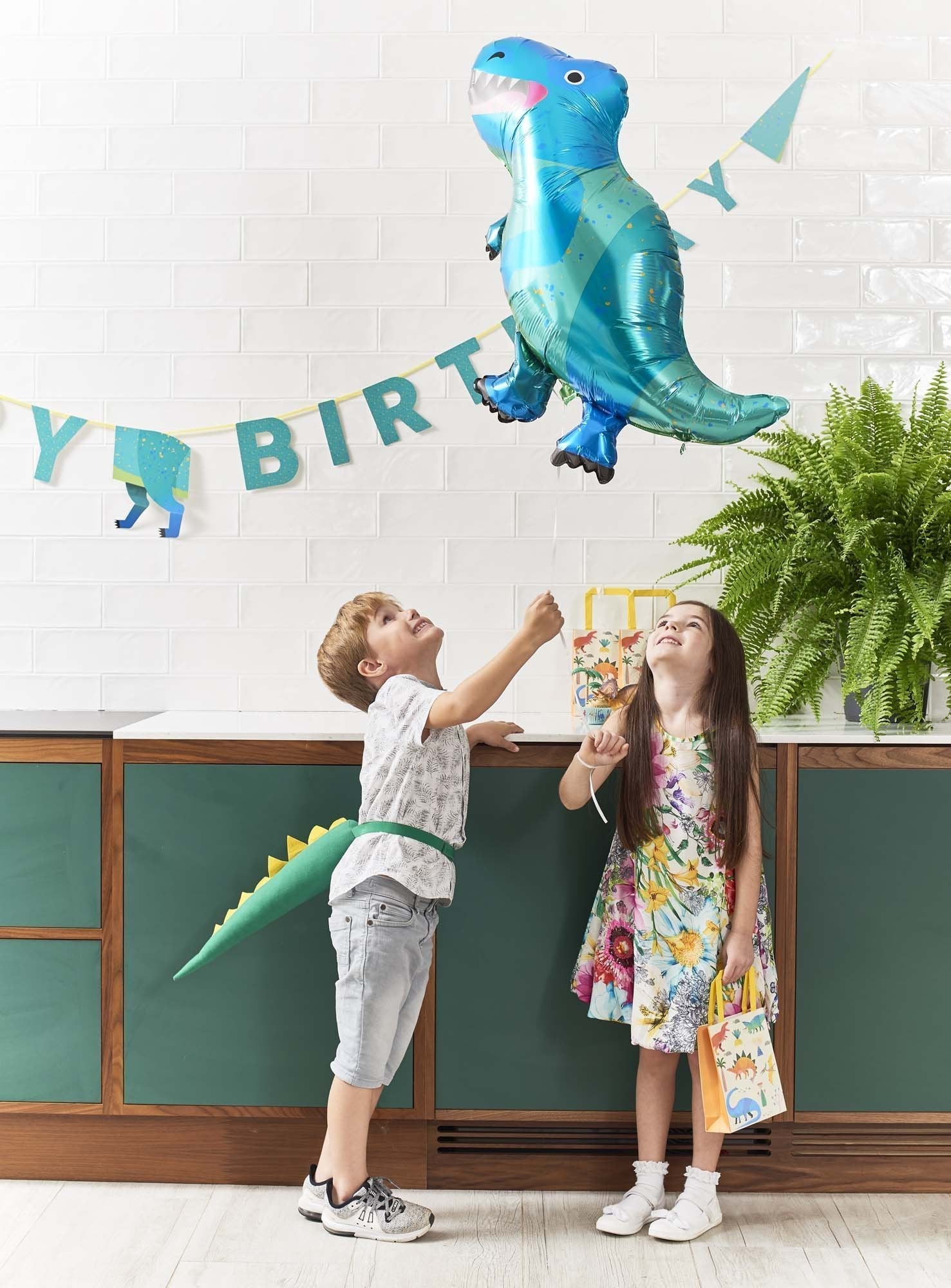 Happy Birthday dinosaur banner and children holding a blue dinosaur balloon
