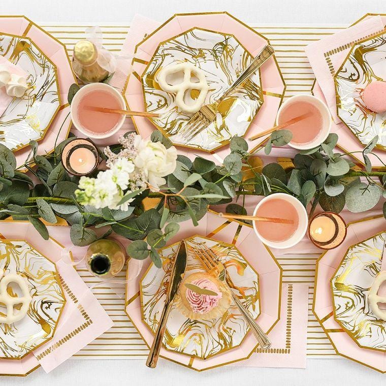White paper table runner with gold pinstripe under assortment of pink and gold party plates and set up